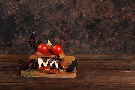 Halloween food concept. Scary burgers with fresh parsley leaves, tomatoes, cream cheese, onion and cutlet on old concrete background, low key, food delivery, cafe advertisement, menu, selective focusの写真素材