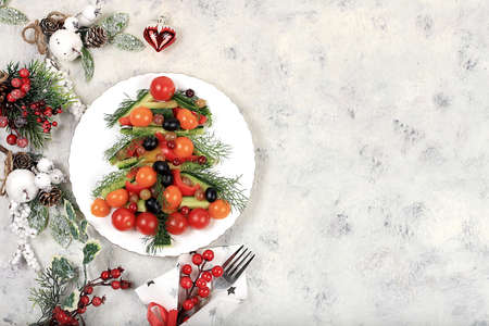 Christmas new year dishes, traditional festive herringbone salad, symbol of the year, prepared from tomatoes, peppers, olives, olives, cucumbers and herbs for vegan food, food design idea, fir branches and decorations,の写真素材
