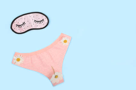 Women's cotton underpants with chamomile flowers and a sleep mask on a blue background with a place...