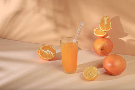 Modern still life with citrus fruits, orange juice and lemon on pastel background with long hard...