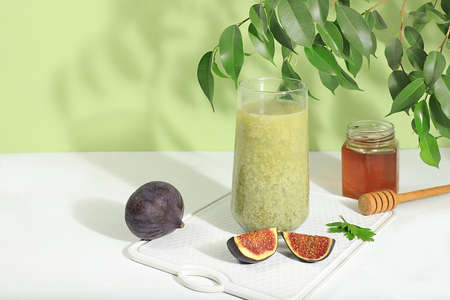 Matcha green tea latte in a glass with figs and honey on a modern light background with tropical leaves. Modern still life on a pastel background with long hard shadows, minimal detox concept, Traditional Indian drink rich in antioxidants used for weight loss and healing, selective focusの写真素材