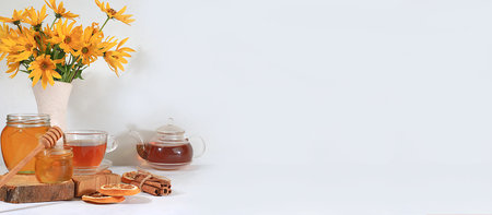 Autumn banner with hot tea in a glass cup, honey and spices on the background of seasonal flowers and leaves, space for text, cozy warm autumn concept, hygge style,の写真素材