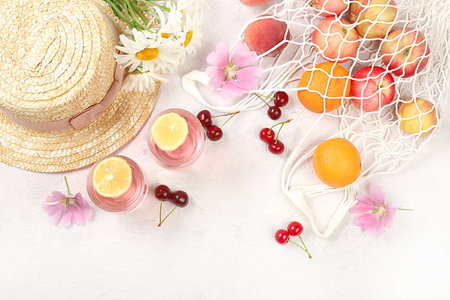 Straw hat,fruits in eco bag,refreshing drinks and chamomile flowers on sunny table.Summer trendy banner on bright background.Vacation and travel concept,outdoor recreation and holiday party.Top view,selective focusの写真素材