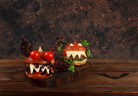 Halloween food concept. Scary hamburgers with fresh parsley leaves, tomatoes, cream cheese, lettuce, onion and cutlet on an old concrete background, food delivery, cafe advertising, menu, restaurant business card, selective focusの写真素材