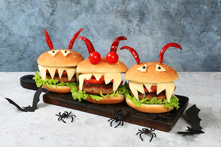 Halloween food concept. Scary hamburgers with fresh lettuce, tomatoes, cream cheese, lettuce, onions, cutlets and peppers in the form of horns on an old concrete background, cafe restaurant business card, selective focusの写真素材
