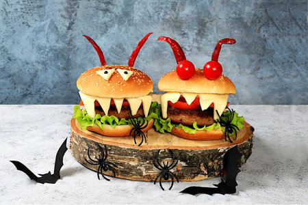 Halloween food concept. Scary hamburgers with fresh lettuce, tomatoes, cream cheese, lettuce, onions, cutlets and peppers in the form of horns on an old concrete background, cafe advertising, menu,の写真素材