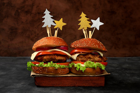 Two Christmas burgers with tomatoes, olives, cream cheese, onions, cutlets on a festive dark table, New Year's food concept. Cafe advertising, menu, restaurant business card, selective focusの写真素材