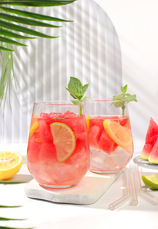 Ice cold homemade lemonade or cocktail with mint, watermelon and fruit, a recipe for a refreshing summer drink. Two glasses with fruit drink on sunny table, detox diet and weight loss concept, menu for restaurant, selective focus.の写真素材