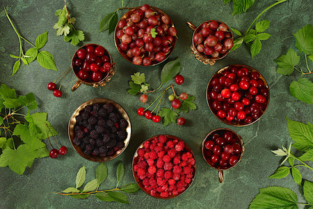 Summer fresh berries of cherry, raspberry, blackberry and gooseberry on green marble background with...