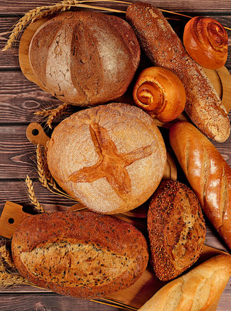 Whole grain homemade bread, different types of round sourdough bread with crispy crust, baguettes, buns and wheat ears, freshly baked bakery products on wooden background, modern baking concept, healthy natural food,の写真素材