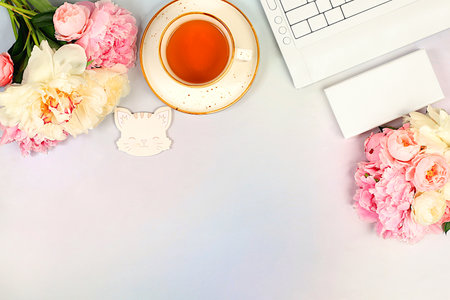 A cozy home table with a laptop, smartphone, tea and a bouquet of delicate peonies and roses. A gift...