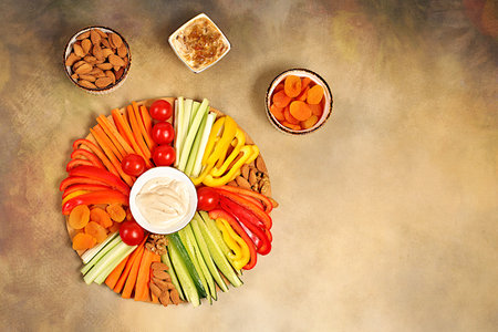 Hummus platter with appetizers, healthy food kitchen background with hummus bowl and raw vegetable sticks, nuts and dried apricots. Middle East plate, traditional vegan appetizers, oriental cuisine concept,の写真素材
