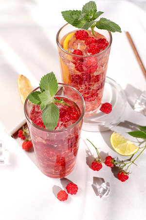 Modern still life with berry juice, raspberries, red currants, mint and oranges on a sunny kitchen...