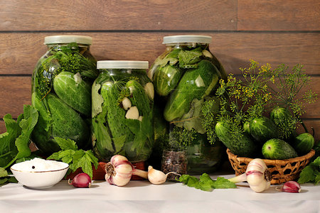 Pickled cucumbers in jars with garlic and dill on wooden kitchen table, rustic collection, homemade...