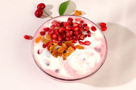Bowl of pomegranate yogurt with pomegranate pieces, raisins and fresh cream for healthy eating on...