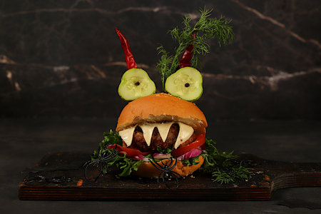 Halloween food ideas. Horrible hamburgers with fresh lettuce, tomatoes, cream cheese, lettuce, onion, cutlets and peppers in the shape of horns on an old concrete background. Halloween food concept, cafe advertising, menuの写真素材