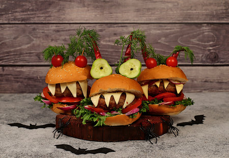 Halloween food concept. Scary hamburgers with fresh lettuce, tomatoes, cream cheese, lettuce, onions, cutlets and peppers in the form of horns on an old concrete background, cafe advertising, menu, restaurant business cardの写真素材