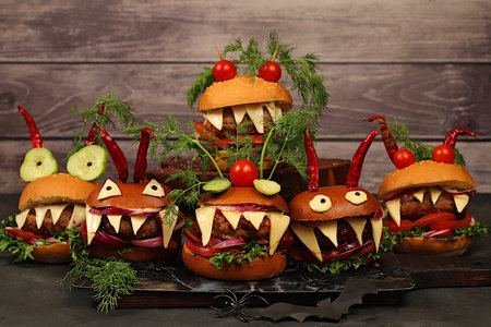 Horrible hamburgers with fresh lettuce, tomatoes, cream cheese, salad, onion, cutlets and peppers in the shape of horns on an old concrete background. Halloween food concept, cafe advertising,の写真素材
