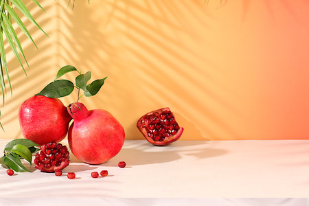 Modern still life with ripe pomegranates on a trendy table in the shade of palm trees, holiday party concept, bar and cafe advertising. Source of vitamins for a healthy lifestyle, autumn banner for a storeの写真素材