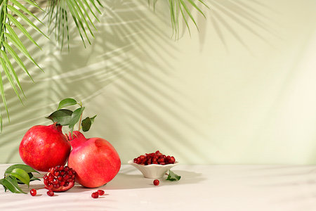 Modern still life with ripe pomegranates on a trendy table in the shade of palm trees, holiday party concept, bar and cafe advertising. Source of vitamins for a healthy lifestyle, autumn banner for a storeの写真素材