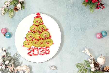 Winter background for greeting card. Edible Christmas tree made of kiwi and pomegranate on the...