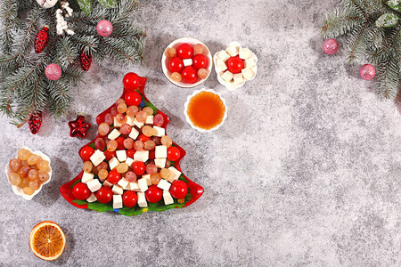 Christmas and New Year's dishes, traditional holiday salad in the shape of a Christmas tree with feta cheese, tomatoes, grapes, olives and honey with fir branches and decorations, dish decoration idea, menu template and banner for a restaurantの写真素材