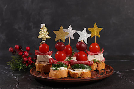 Christmas and New Year's dishes, a set of appetizers for the festive table. Canapes with soft mozzarella cheese, tomatoes, salami, grapes, and olives on a dark table, Christmas Eve concept.の写真素材