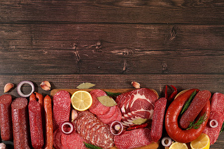 Selection of various smoked and dry-cured sausages, sliced salami, and spices on a kitchen counter. Advertising and menu for a store, banner for a cafe or restaurant. Delicious, aromatic holiday appetizers, design template.の写真素材