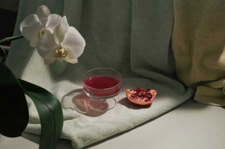 Sunny composition with drapery, orchids and red pomegranate and glass.の写真素材