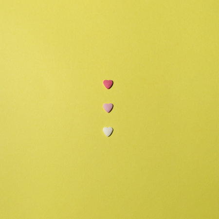 Three hearts of different colors in a row on yellow background. Minimalist composition.の写真素材
