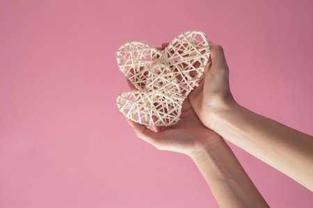 Two hearts and hand holding them on a pink background. Minimalist idea.の写真素材