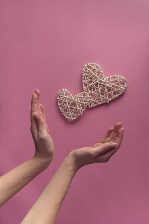 Two hearts and the hand holding them on a pink background. Minimalist idea.の写真素材
