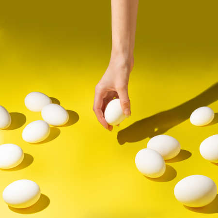 Easter modern composition. Hand is putting egg on yellow background.の写真素材