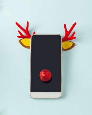 Reindeer horns on the phone with a red nose on blue background. New Year's mood.