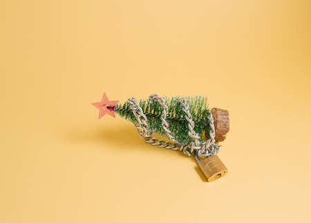 Layout with a Christmas tree with chain and padlock on yellow background. New Year mood in covid...