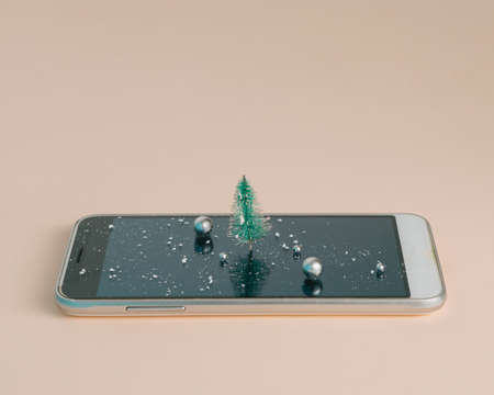 Cell Phone with Christmas tree, snow and shine balls on pink background.