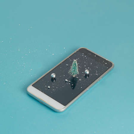 Cell Phone with Christmas tree, snow and shine balls on blue background.