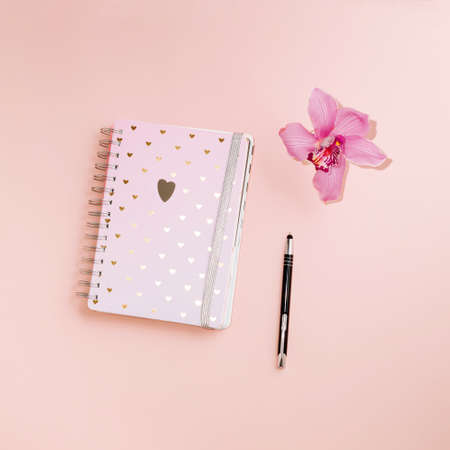 A notebook with hearts lying on a pink background with a pink orchid and a pencil. Notes, thoughts, plans ...の写真素材