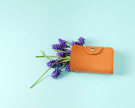 The wallet from which the purple flowers protrude lies on a turquoise background.