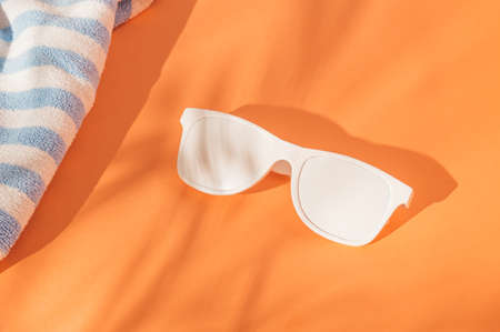 Sunglasses and a blue and white towel lie on a sandy orange background.  The concept of summer, sunbath rest and enjoyment.の写真素材