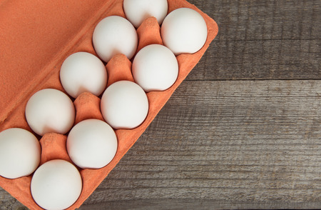 Colorful carton of organic white eggs with easter decor on wooden board. Top view.