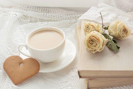Cup of coffee with cookies as heart and book with dry rose on lace. Vintage.の写真素材