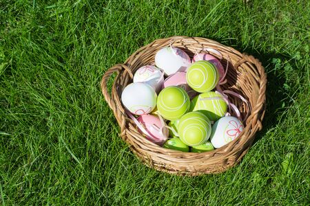 Easter painted pastel color eggs with ribbon in basket on green grass. Sunny day. Close up. Selective focus.の写真素材