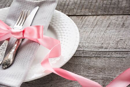 Elegance table setting with pink ribbon for romantic dinner on wooden board. Rustic stile. Close up.の写真素材
