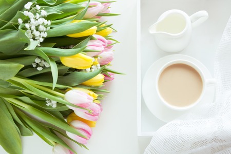Morning breakfast in spring with a cup of black coffee with milk and pastries in the pastel colors, a bouquet of fresh yellow and pink tulips on a white background. Top view.の写真素材