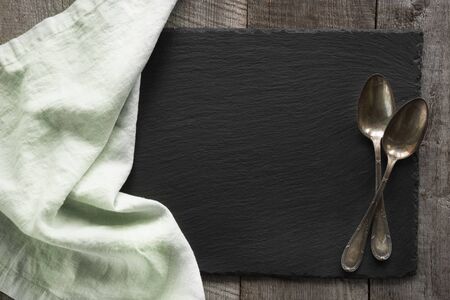 Green linen napkin and vintage spoons on black slate dish. Top view. Space for your text.の写真素材