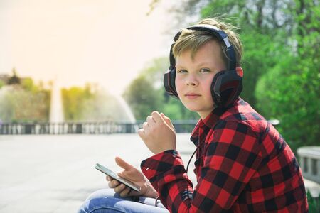 Handsome teenager surfing the net while sitting on a longboard and listening to music.の写真素材
