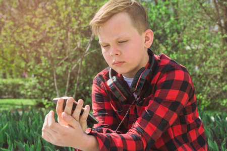 Handsome teenager surfing the net while sitting in park.の写真素材