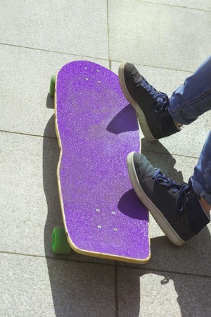 Close up of teens leg in blue sneakers resting after extreme ride wooden longboard. Vertical.