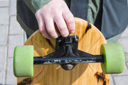 Teen hold longboard with green wheels in hand. Close up.